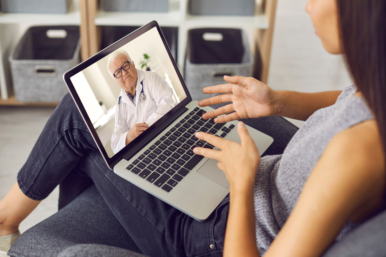 Young Woman Using Laptop and Talking to Experienced Senior Doctor during Online Video Consultation